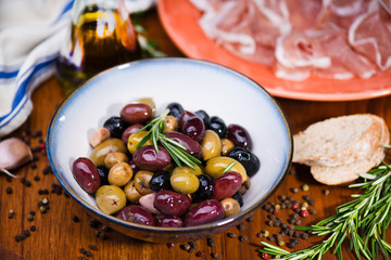 Olives in bow with prosciutto on wooden table