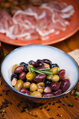 Olives in bow with prosciutto on wooden table