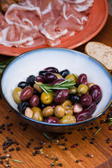 Olives in bow with prosciutto on wooden table