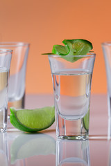 Tequila shot with a slice of lime on the glass orange background