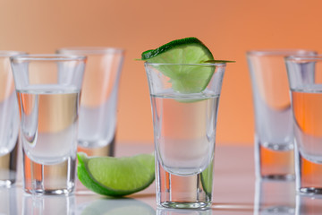 Tequila shot with a slice of lime on the glass orange background