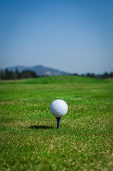 Golf ball on teeing area with green grass ahead and mountains in