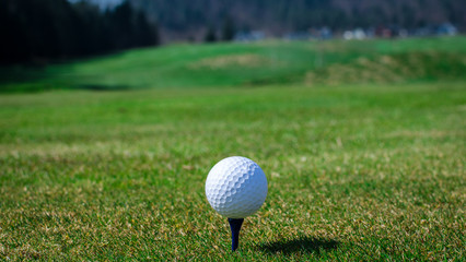 Golf ball on teeing area with green grass ahead and mountains in