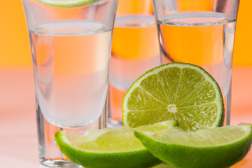 Tequila shot with a slice of lime on the glass orange background