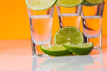 Tequila shot with a slice of lime on the glass orange background