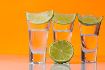 Tequila shot with a slice of lime on the glass orange background