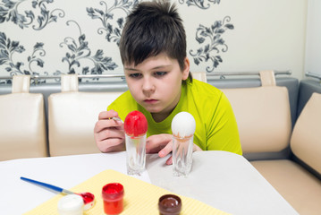 boy paints the Easter eggs with a brush