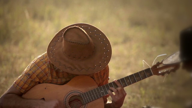 Romantic cowboy in hat is playing acoustic guitar and sing song