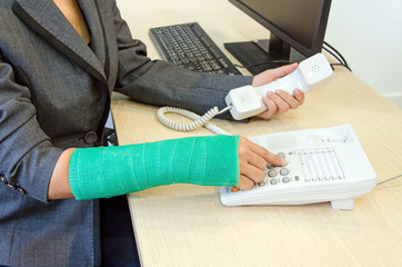 Injured businesswoman with green cast on the wrist pressing numb