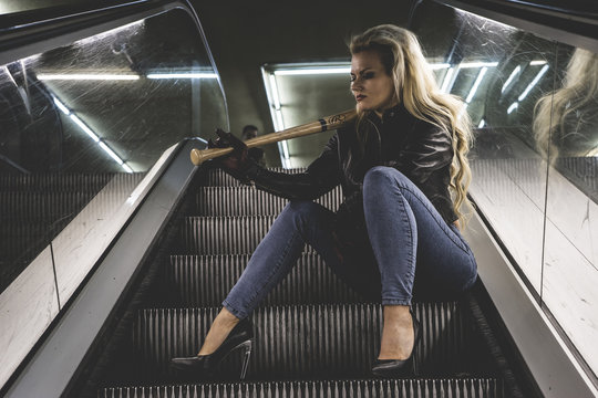 Urban beautiful blonde with a baseball bat in escalators