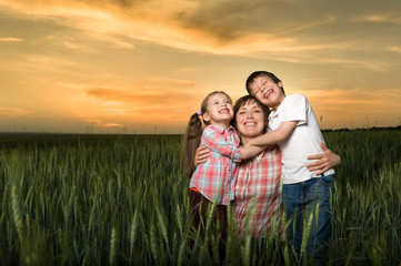 happy mother and childs in green field at sunset