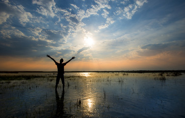 Man holding arms up in praise in sunset  while being in water