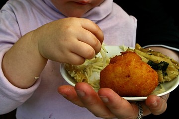 2 years old girl taking noodles from dish held by adult hand