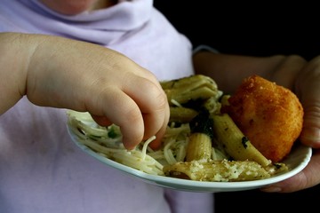 Hand of small girl taking noodles from plate held in adult hand