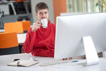 Handsome businessman in eyeglasses is using a computer, talking on the mobile phone and smiling while working in office