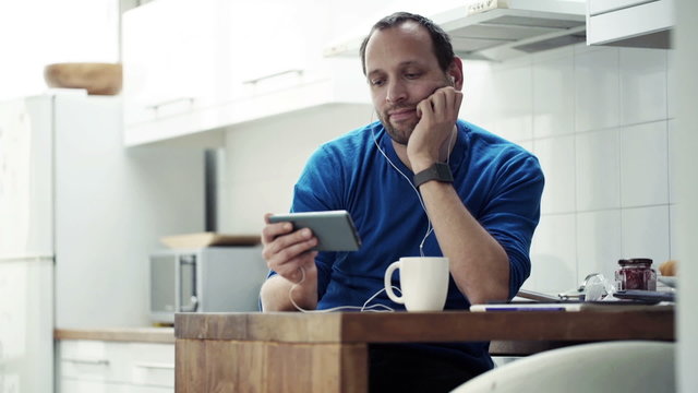 Man watching movie on smartphone and drinking coffee by table