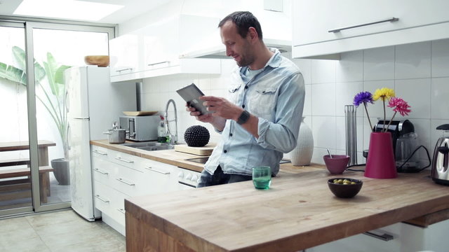 Happy, young man playing on tablet computer standing by table