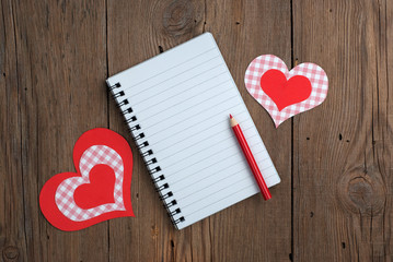 Notebook with hearts and pencil on old wooden table