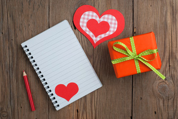 Notebook with gift, pencil and hearts on old wooden table