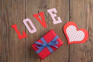 Gift and paper hearts on old wooden background