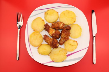 Baked and sauced chicken drumsticks surrounded by potatoes