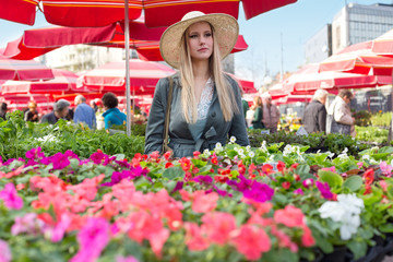 Fototapeta premium Attractive blonde woman with straw hat on flower marketplace.