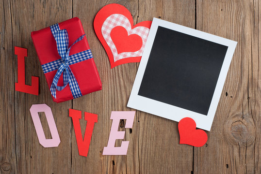 Instant photo with gift and hearts on old wooden background