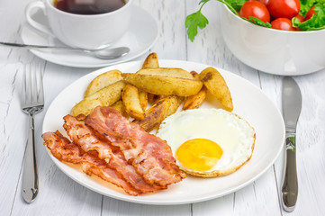 Hearty breakfast with bacon, fried egg, potato and cup of coffee