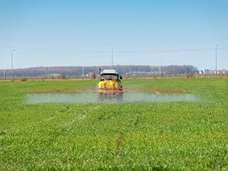 tractor spreading herbicides over a green field