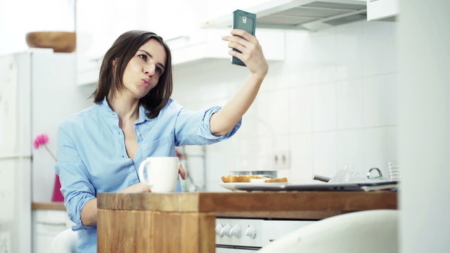 Young woman taking selfie photo with cellphone sitting by table