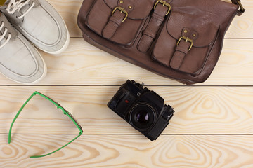 leather bag, camera, glasses, gumshoes on wooden table
