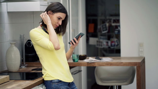 Young, Pretty Woman Using Smartphone Standing In Kitchen 