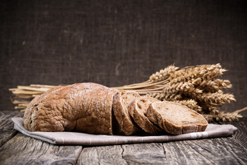 Tasty bread with wheat on wooden background.