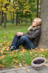 Sad girl sitting under the tree in the autumn park