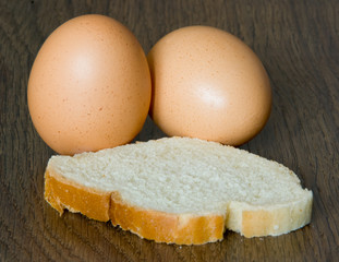 Two whole eggs and pce of white bread on a dark brown board