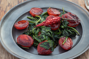 Fried tomatoes with spinach leaves and chili.
