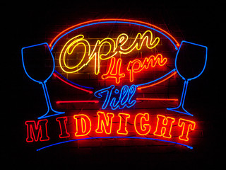 Red, green, purple and yellow neon sign of the words 'open 4pm t
