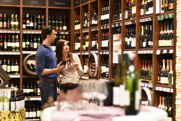 young couple buys a bottle of red wine in the store - obrazy, fototapety, plakaty