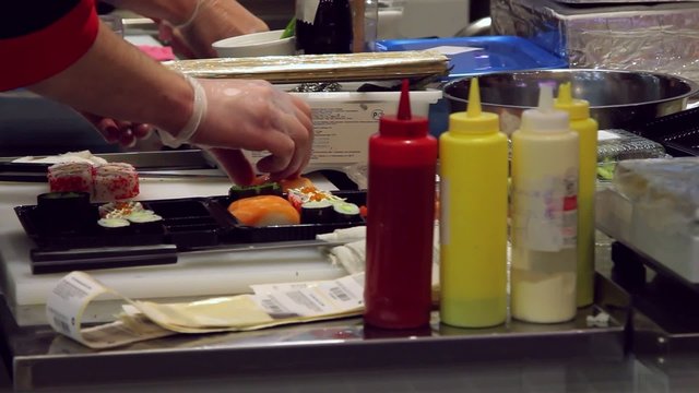 Close up of sushi chef hands puts in a container for sale In