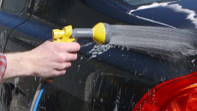 Car Care - Man using a garden spray gun to remove the soap