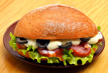 Sandwich with ham, vegetables and olives on wooden background