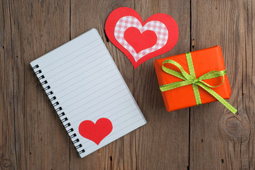 Notebook with gift and hearts on old wooden table
