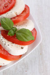 Tomato and mozzarella with basil leaves on a white plate