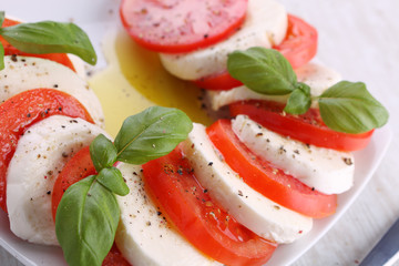 Tomato and mozzarella with basil leaves on a white plate