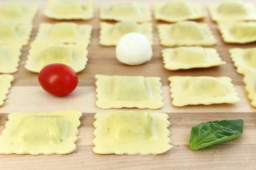 Ravioli arranged in a row with tomato, bocconcini and basil