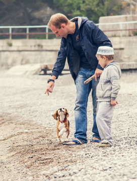 Father and son playing wirh little puppy on the seaside