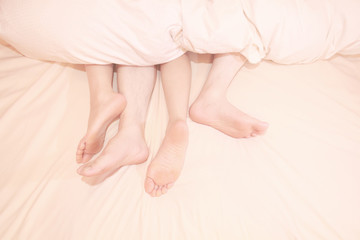 Two pairs of feet under the covers at home in bedroom