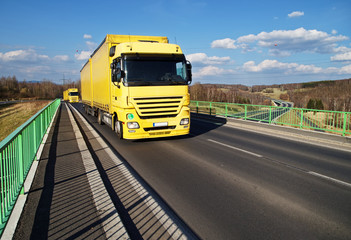 Two yellow trucks driving across the bridge over the motorway
