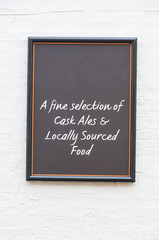 Isolated noticeboard for a pub on a white painted brick wall