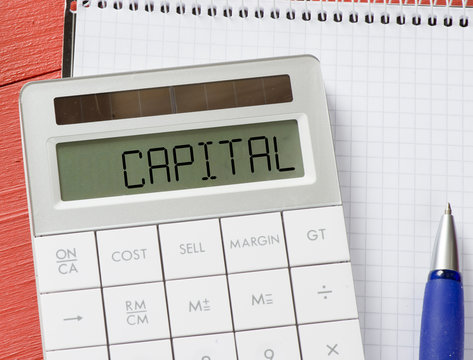 Calculator with word catipal and notepad, pen on background